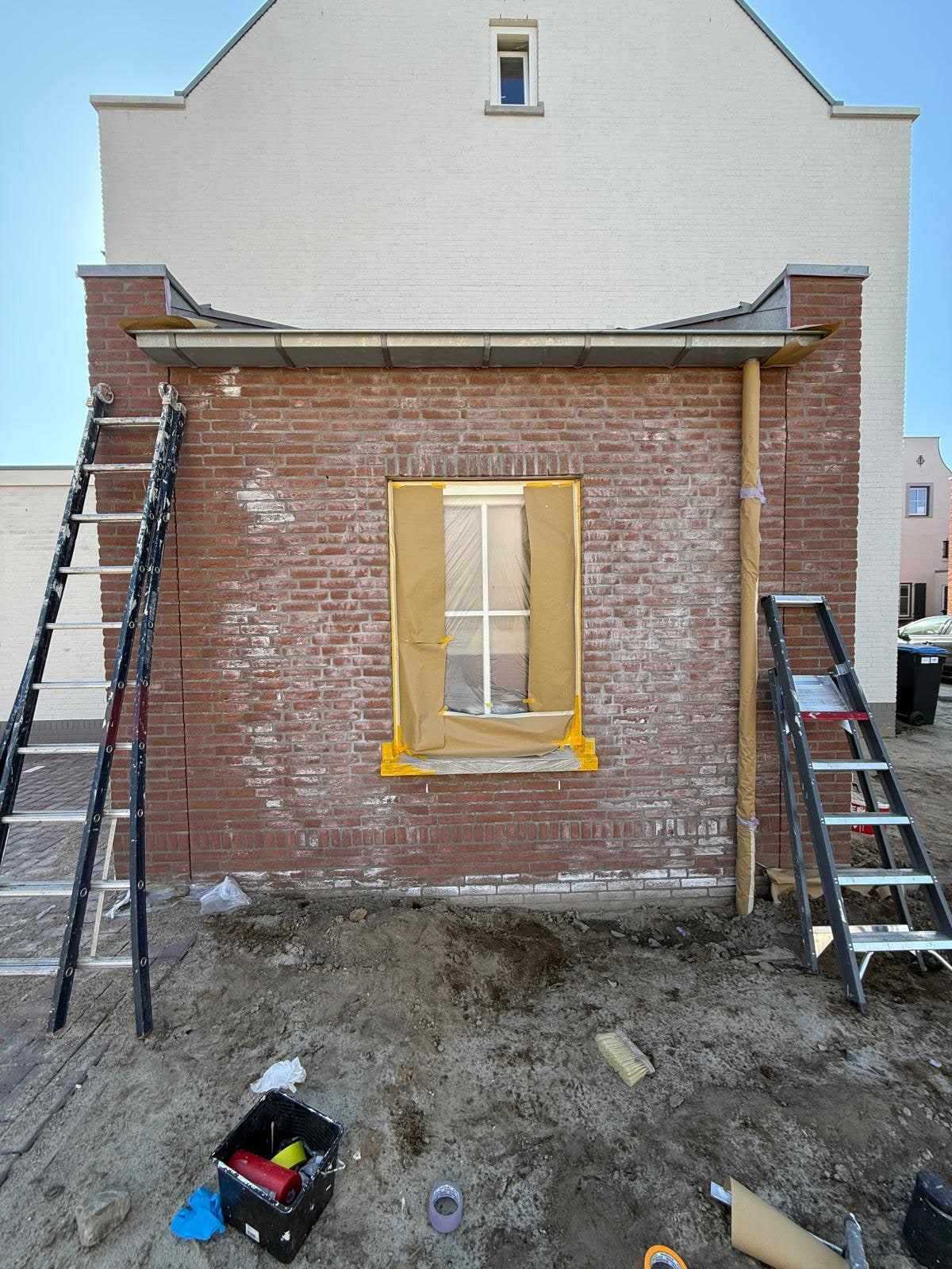 Rode bakstenen aanbouw met een afgeplakt raam en ladders, nog niet geschilderd