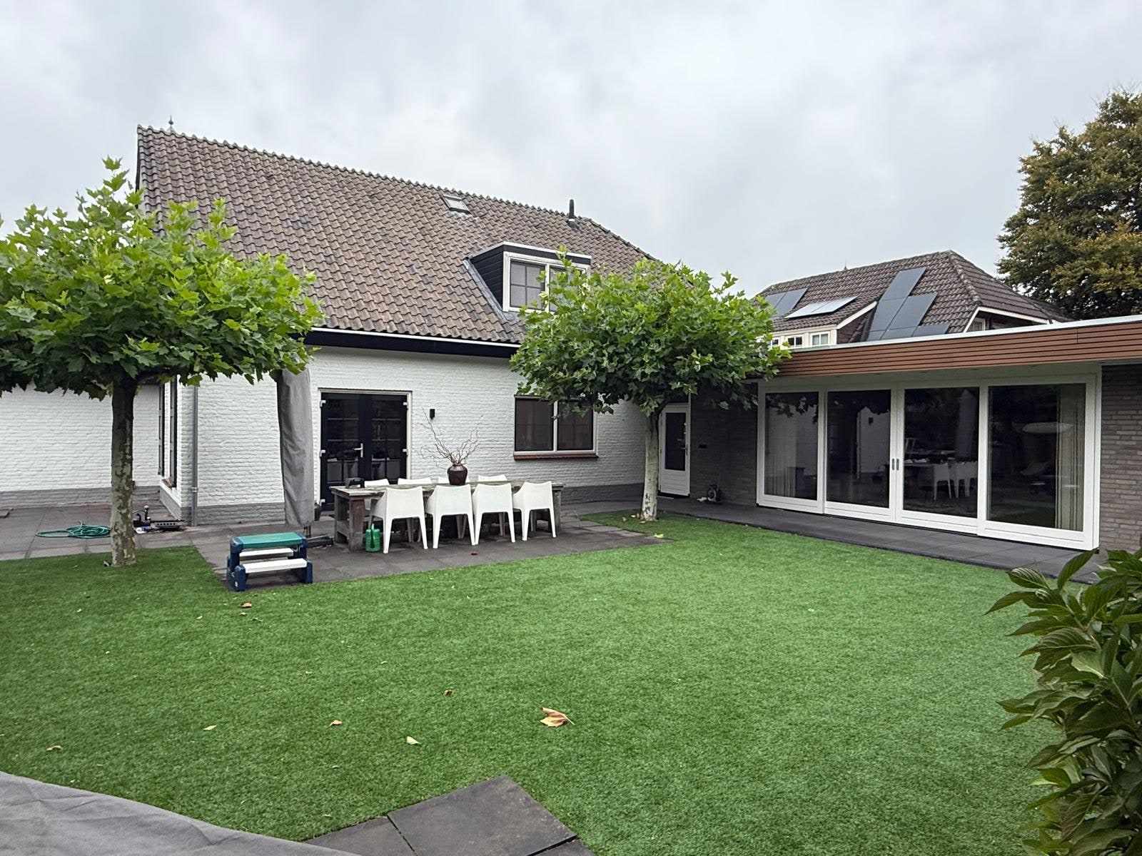 Tuin met kunstgras en het terras langs de wit geschilderde achtergevel