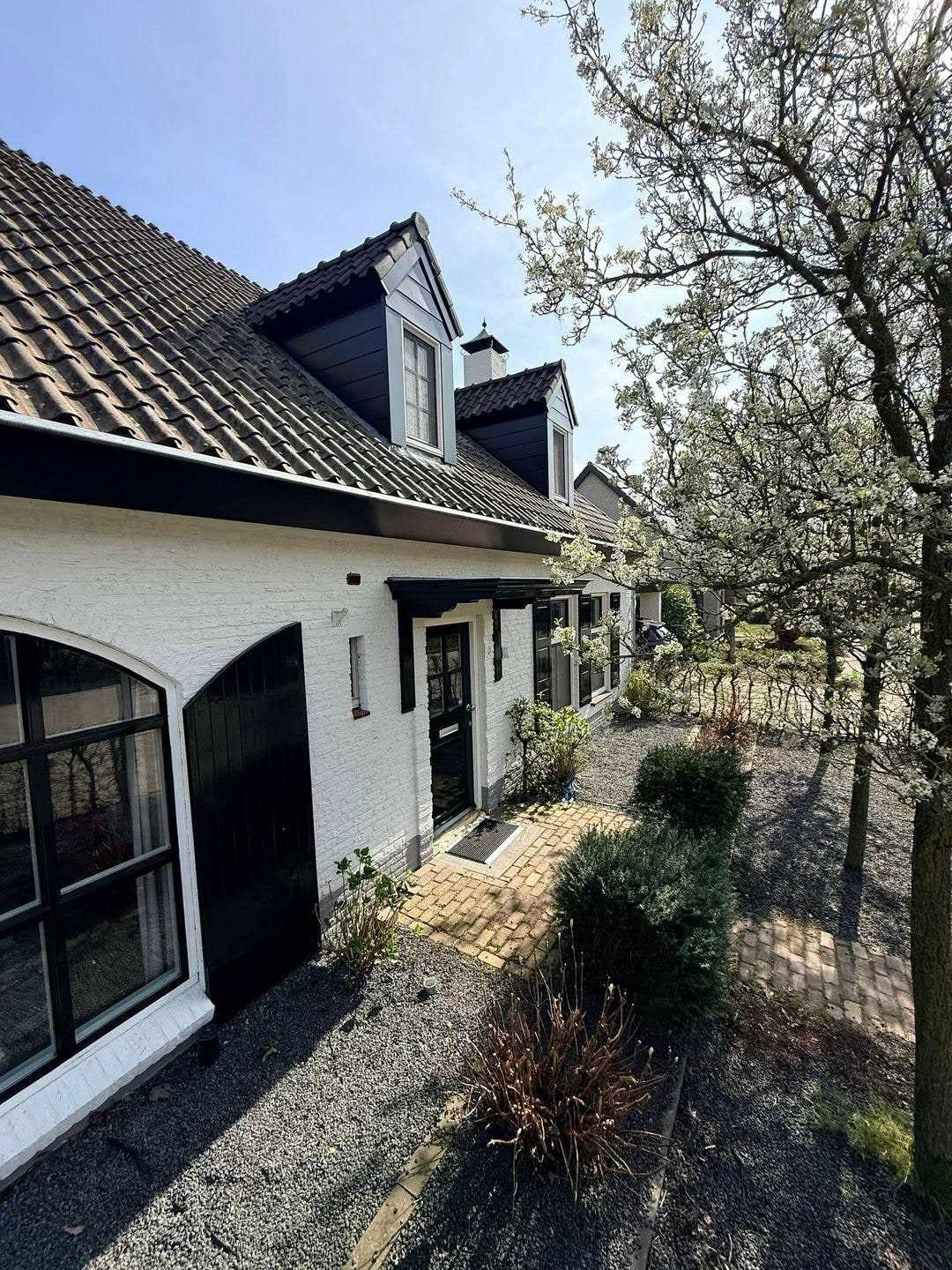 Zijgevel van de witte woning met donkere garagedeur en een grindpad ernaast