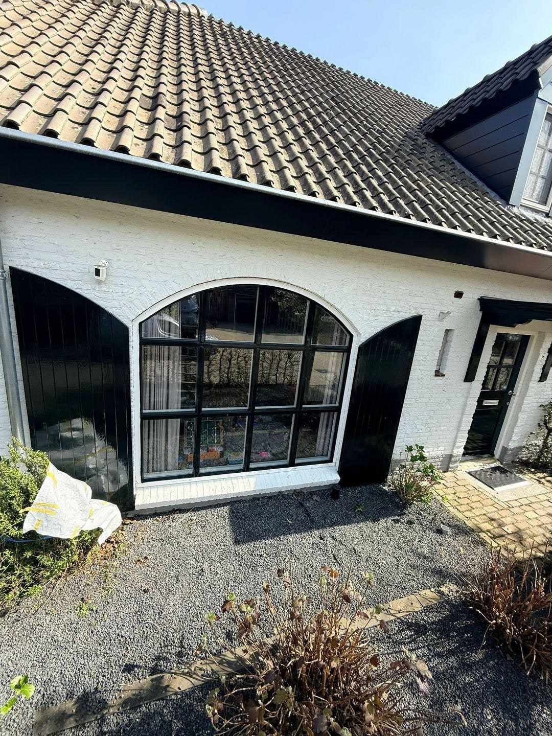 Boogvensters met zwarte roeden onder een pannendak in de witte gevel