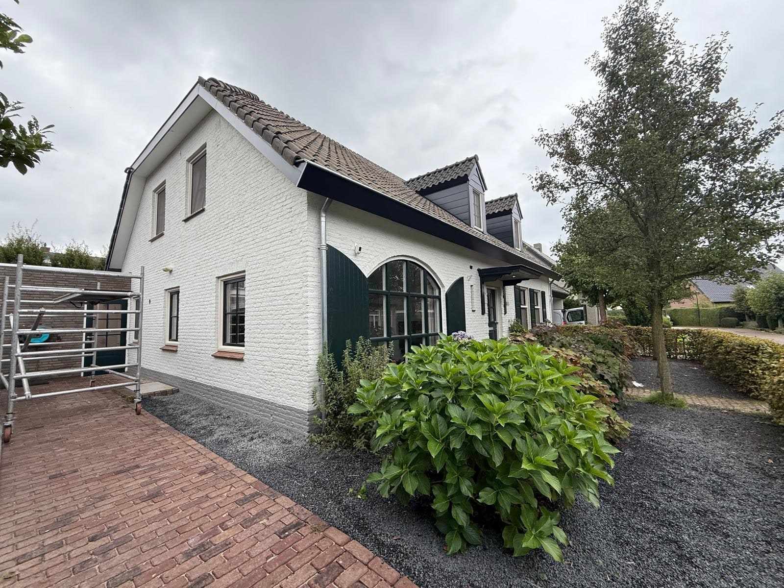 Wit geschilderde woning met donkergroene luiken, gezien vanaf het klinkerpad