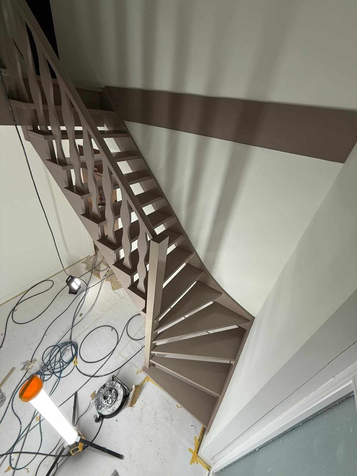 Trap in taupe gelakt tegen een witte wand, met kabels en een lamp op de vloer