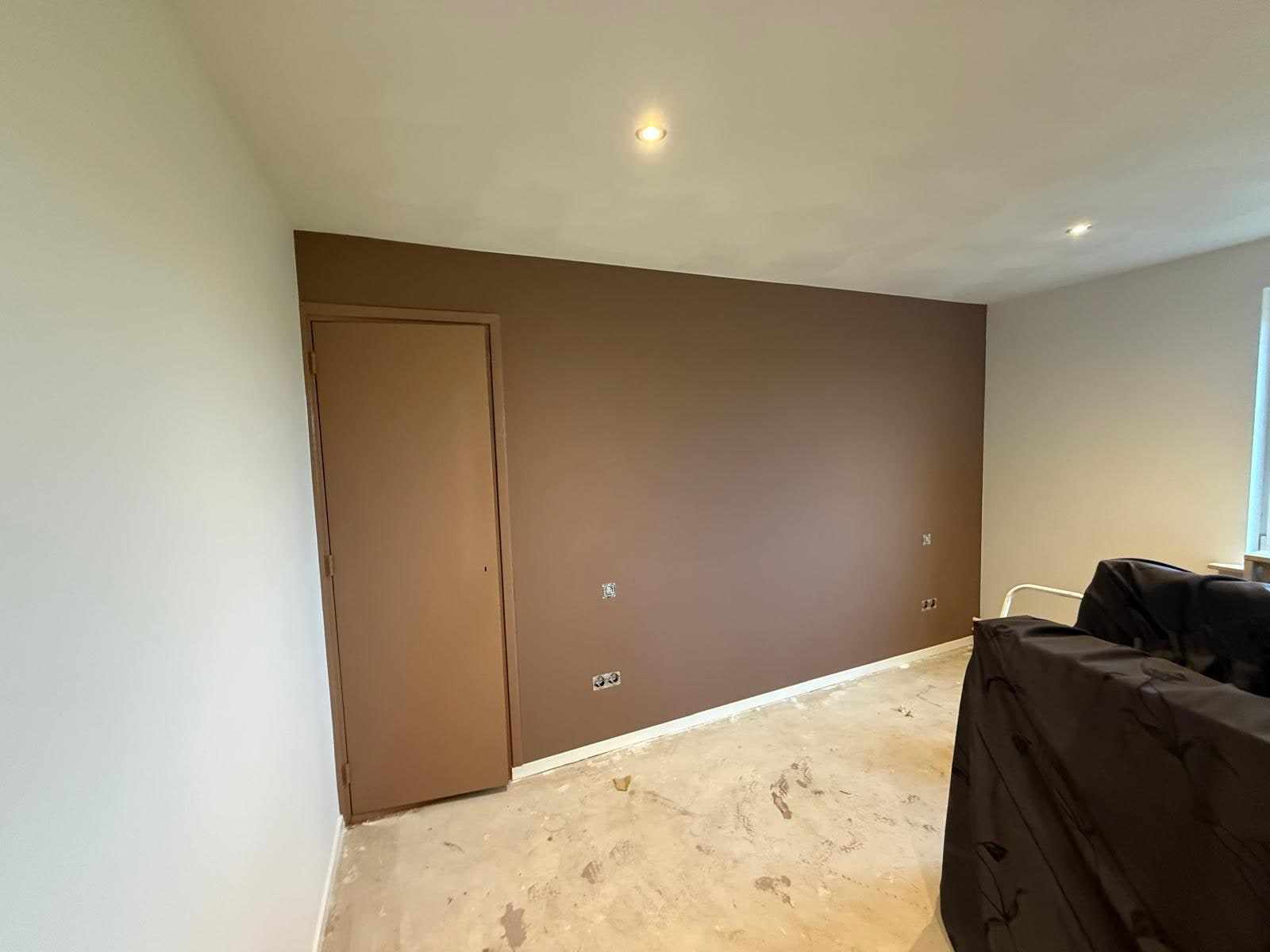 Taupe geschilderde wand met deur, meubels ervoor afgedekt met folie
