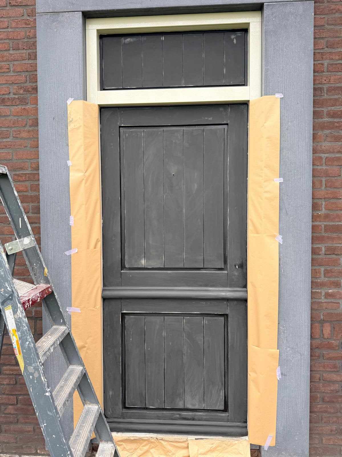 Donker geschilderd deurpaneel in de bakstenen gevel, het kozijn nog afgeplakt