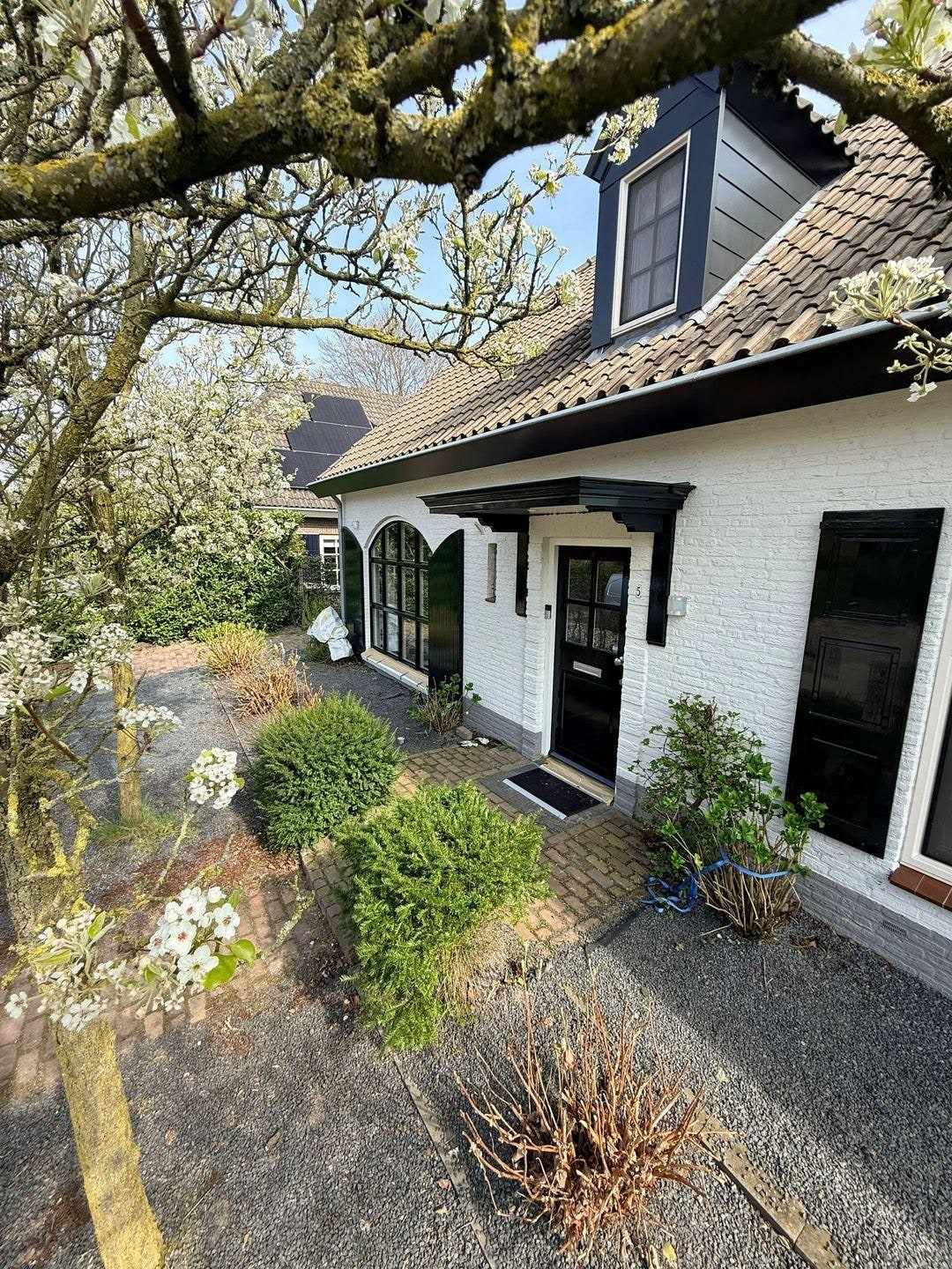 De witte woning in de lengte gezien vanaf het grindpad, onder een bloeiende boom