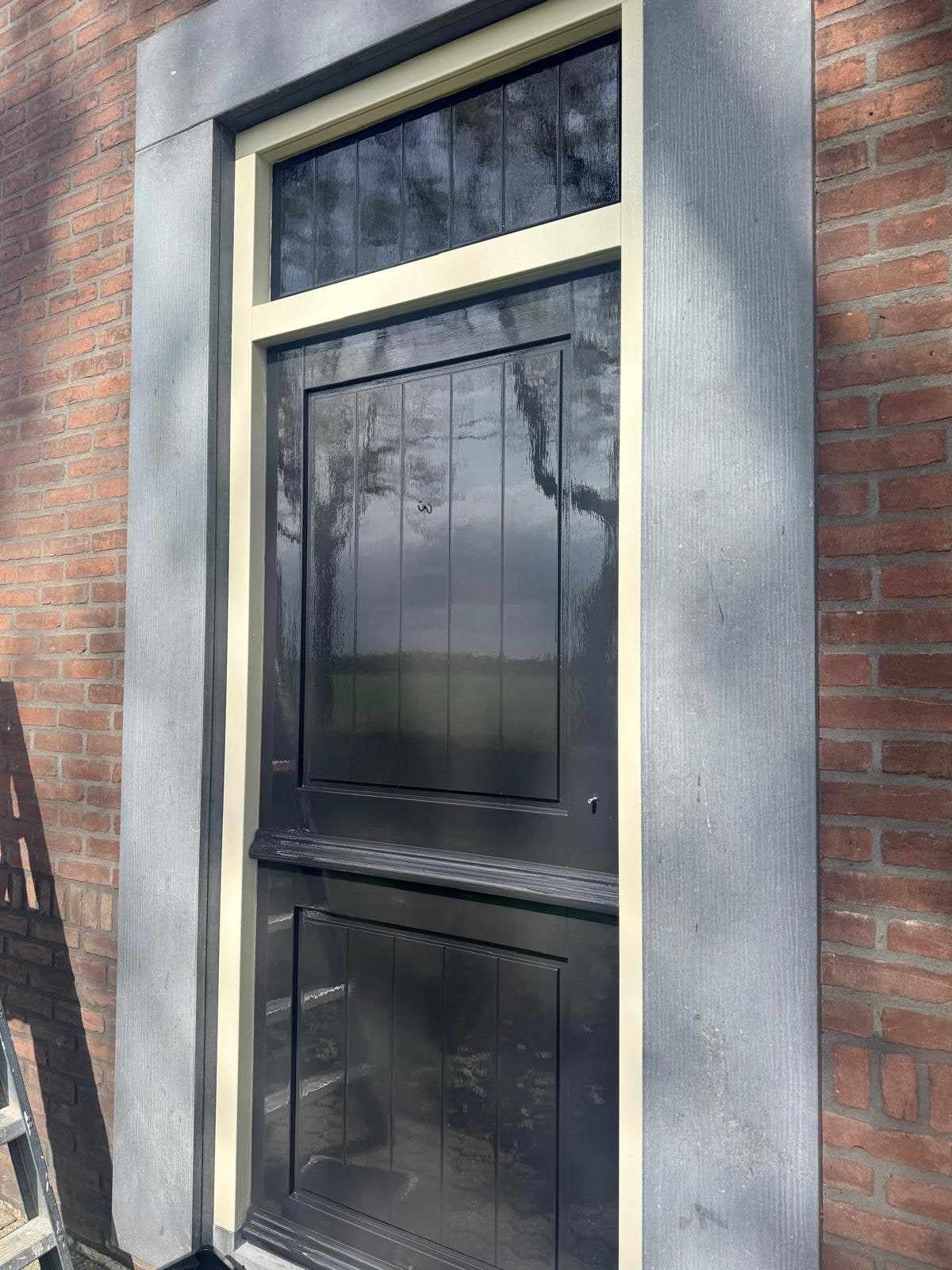 Zwart geschilderd raamkozijn met roeden, van opzij gezien tegen het metselwerk