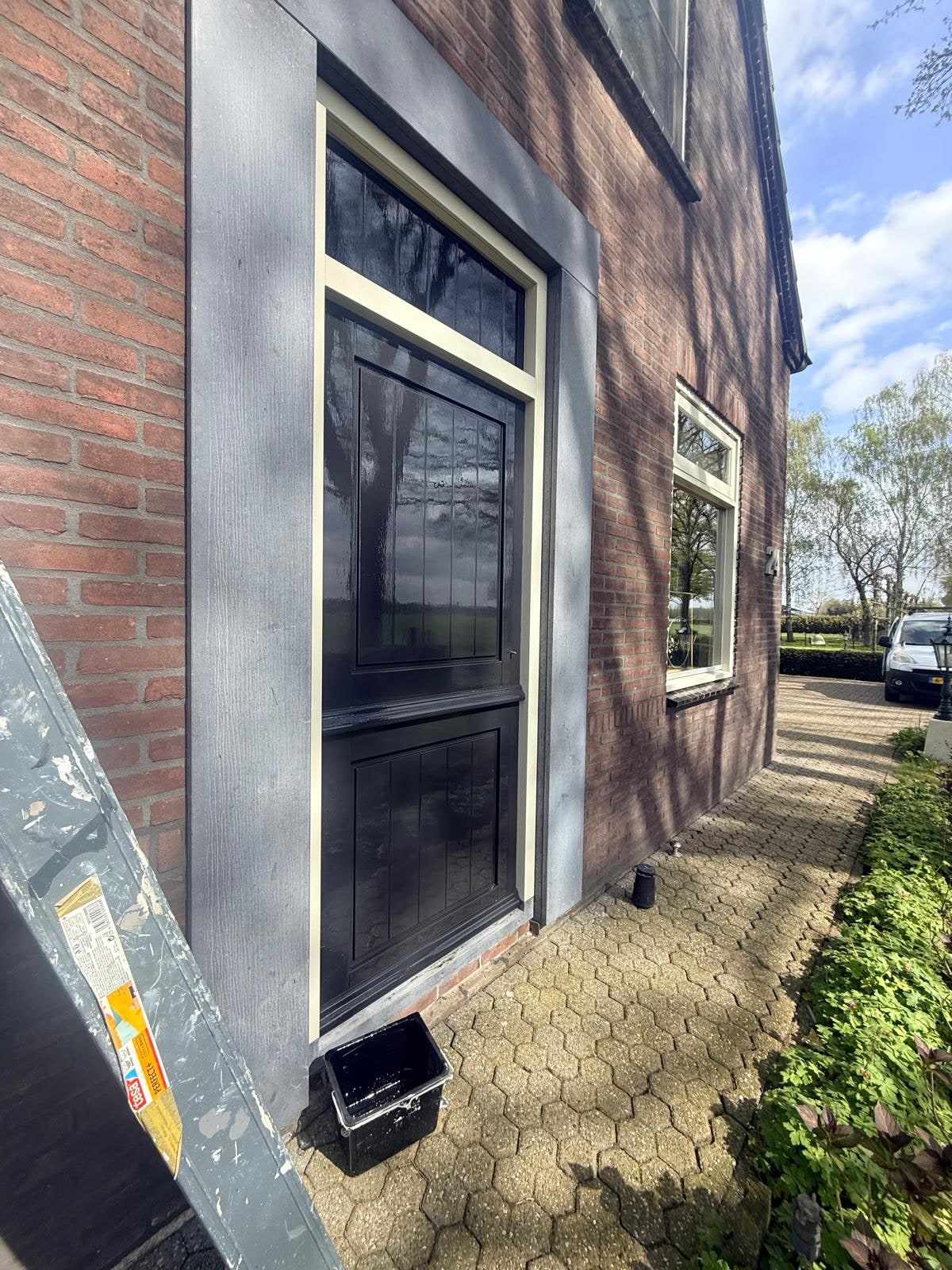 Zwart gelakt hoekraam met een ladder ernaast langs de zijgevel