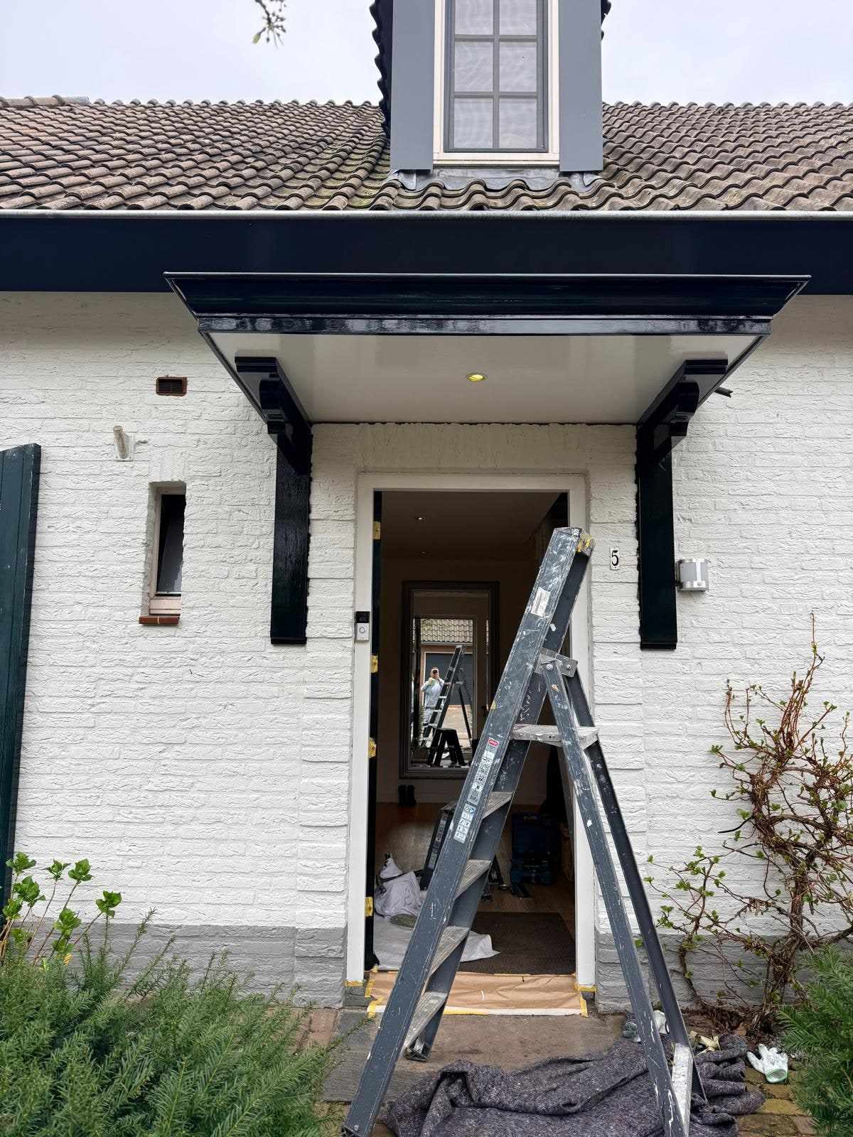 Entree afgedekt met een dekzeil en een ladder tegen de gevel tijdens het schilderen