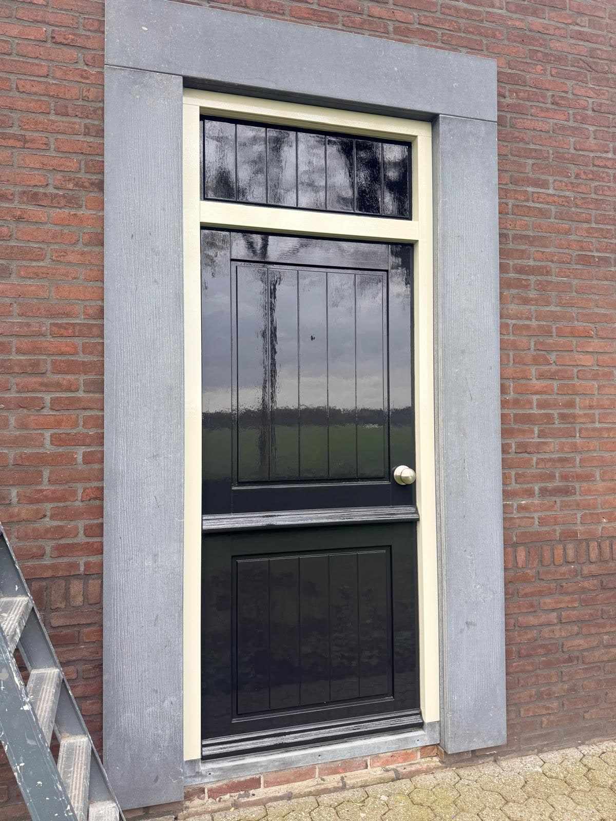 Zwarte voordeur met glas-in-lood bovenlicht in een licht geschilderd kozijn